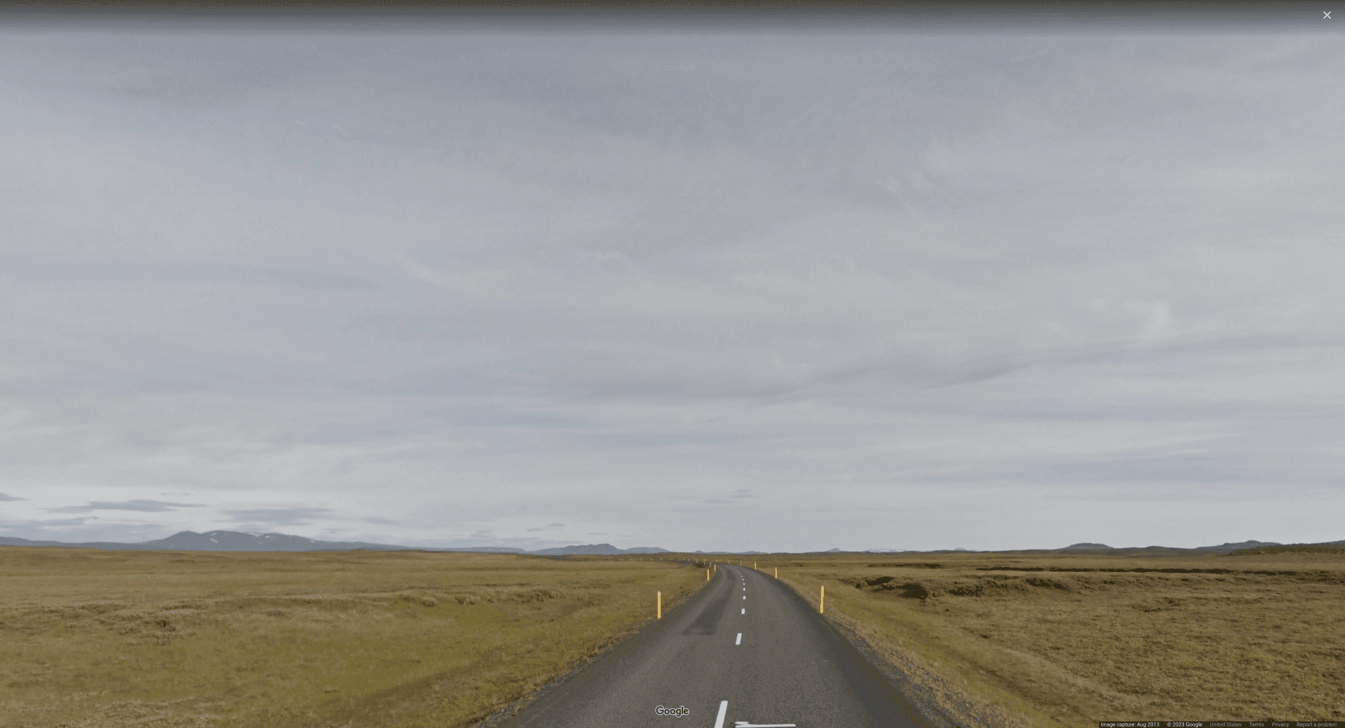 Picture of a road in an extremely flat & empty plains, with overcast skies and yellow reflector poles